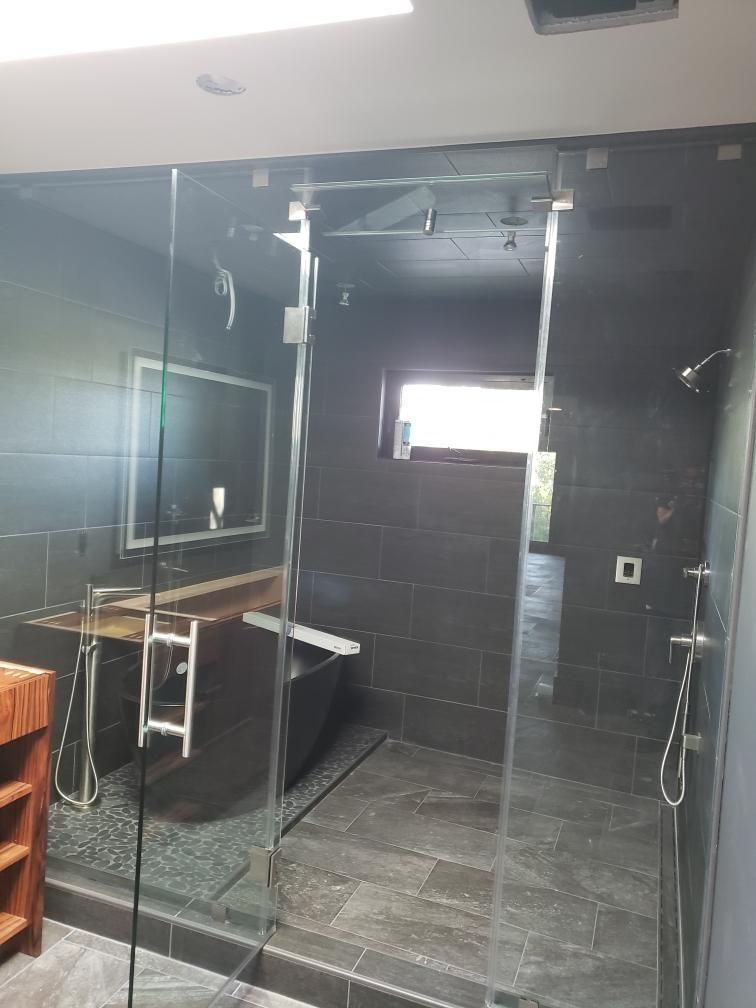 A modern bathroom with a large glass shower, dark tile walls, a bathtub, and wooden accents.