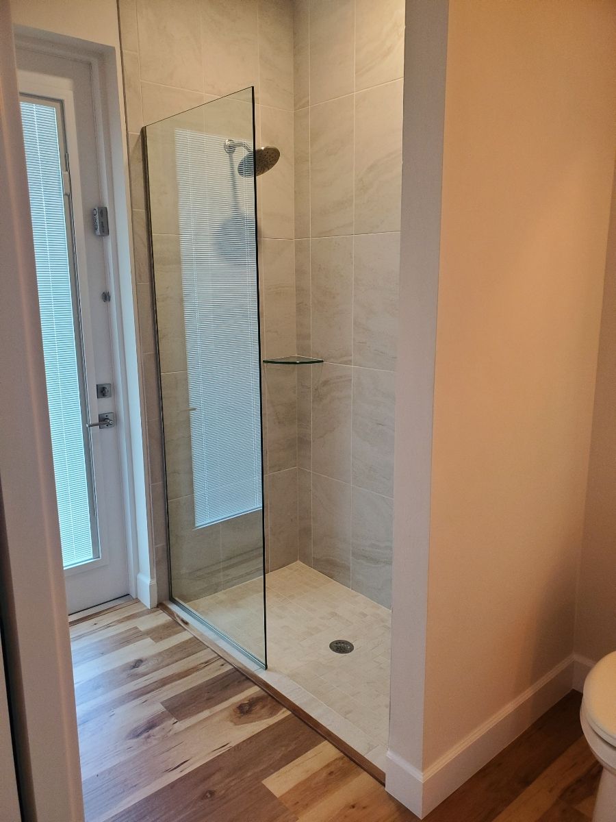 Shower with glass door, tiled walls, and wooden floor. Door to outside is visible.