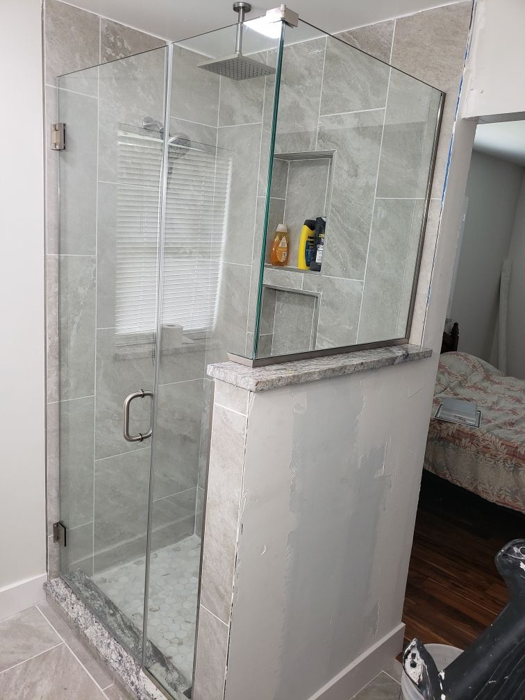 Glass-enclosed shower with tiled walls, built-in shelves, and a granite ledge.