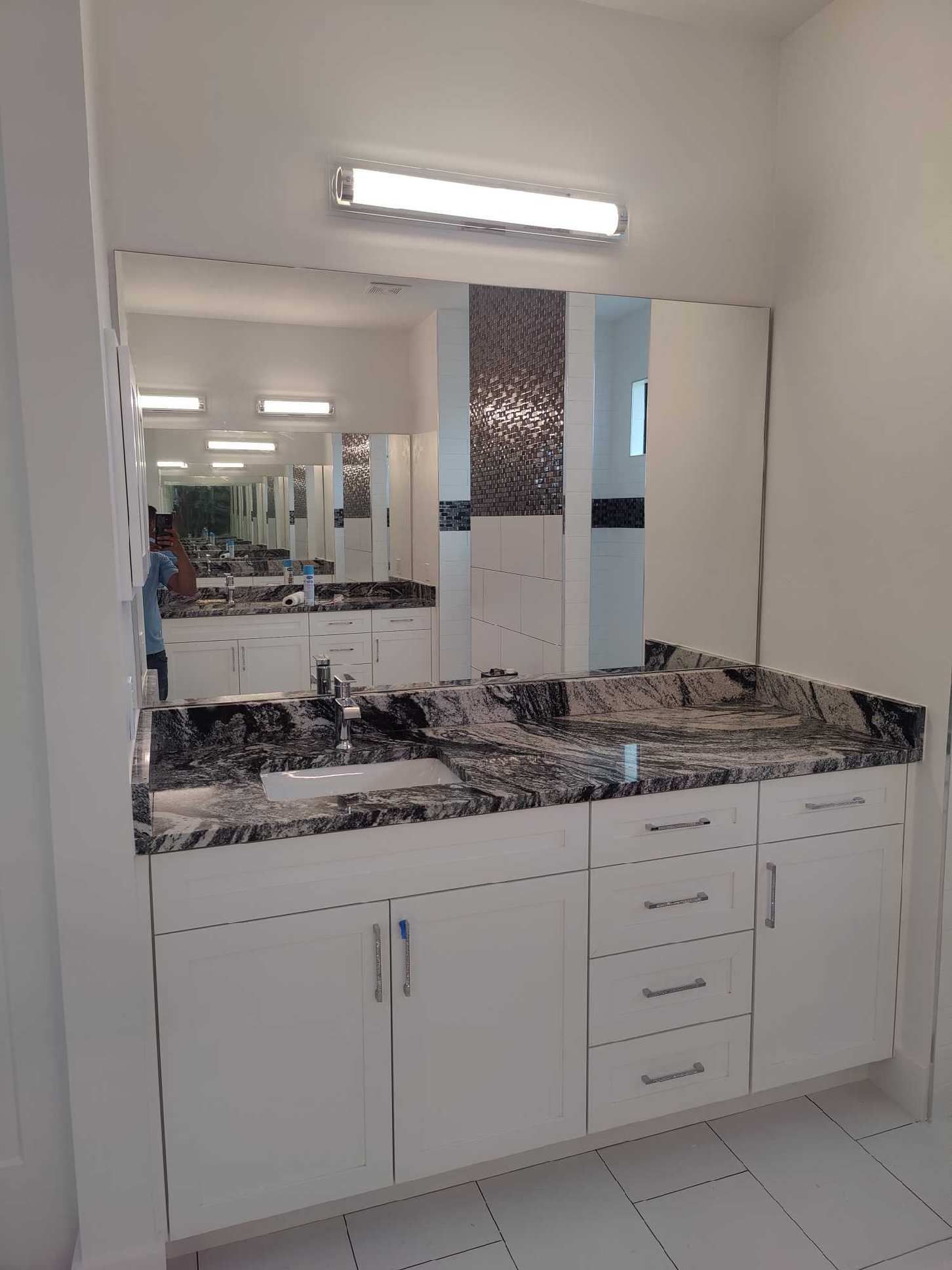 Bathroom with white cabinets, black granite countertop, large mirror, and mosaic accent.