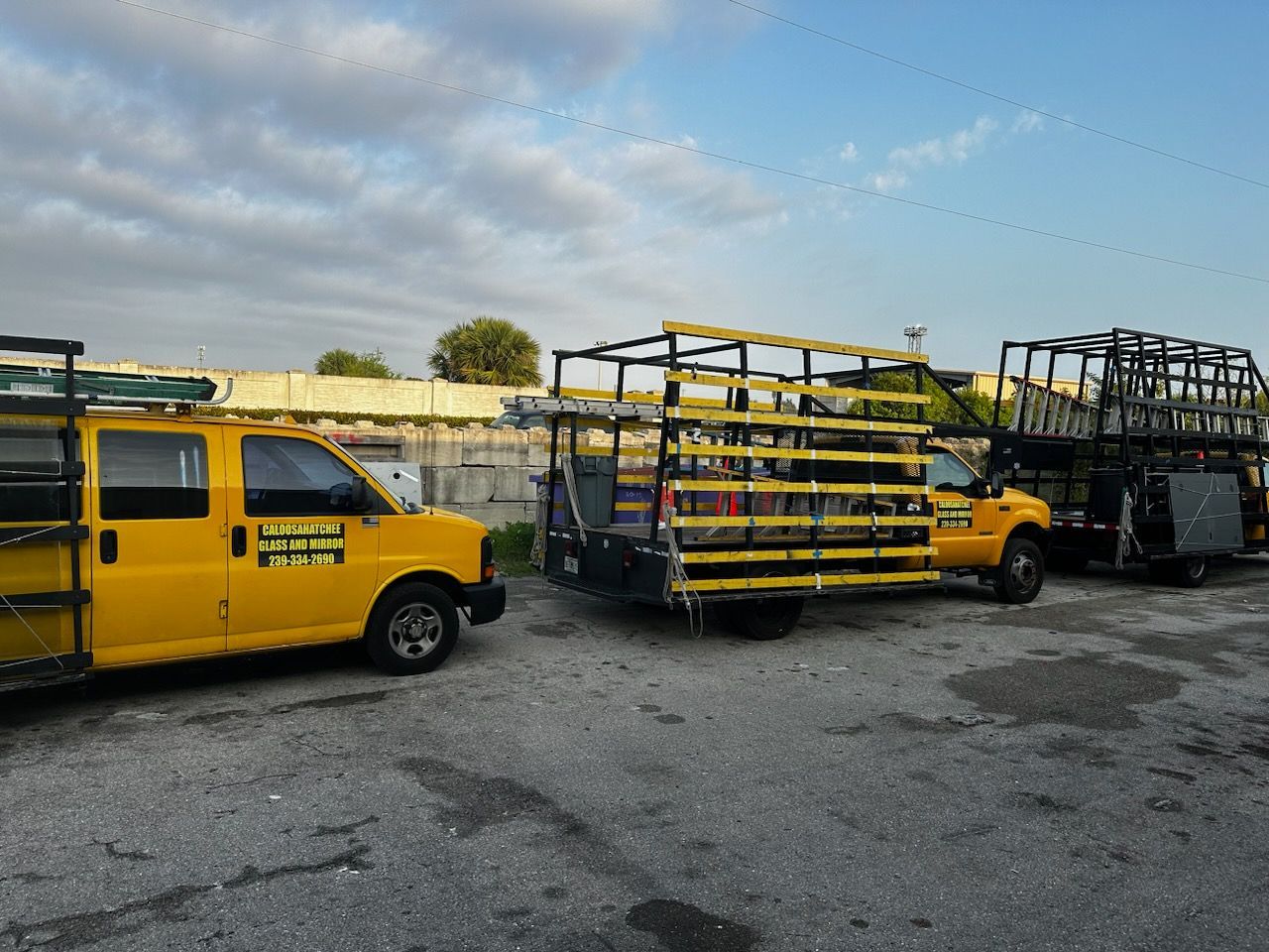 Yellow work trucks with black frames parked on a grey lot; cloudy sky background.