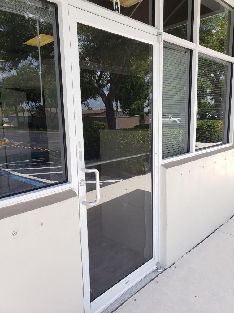 Glass door with white frame, next to windows, reflecting trees and building exterior.