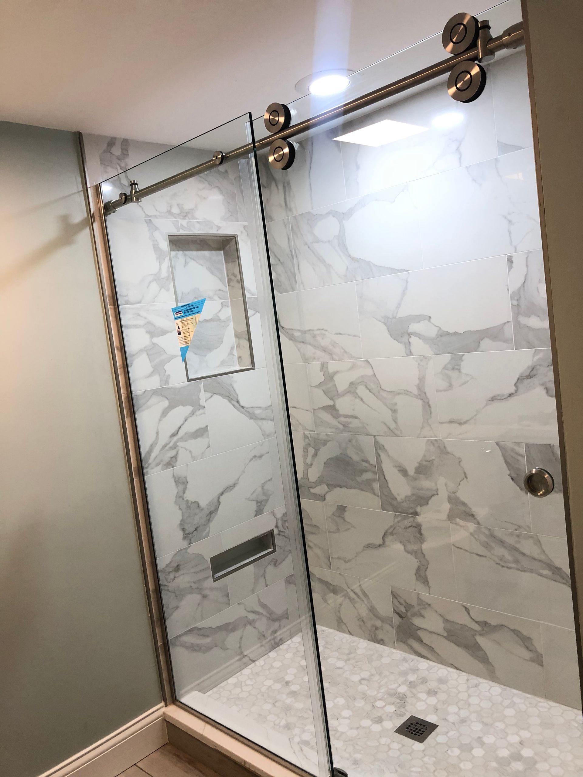 A modern shower with sliding glass door, marble tile walls, and a built-in soap niche.