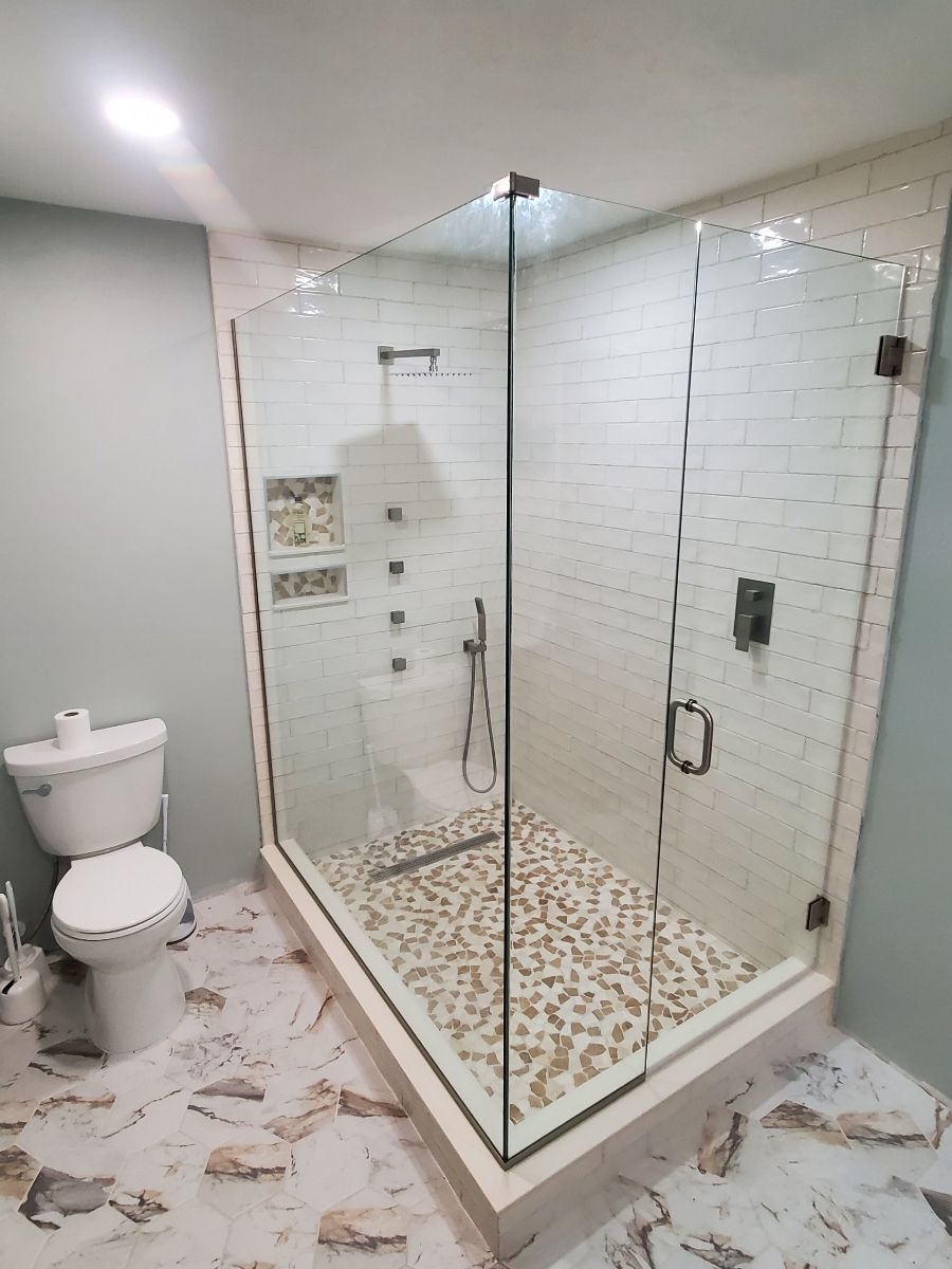 A modern bathroom with a glass-enclosed shower, white and stone tile, and a toilet.