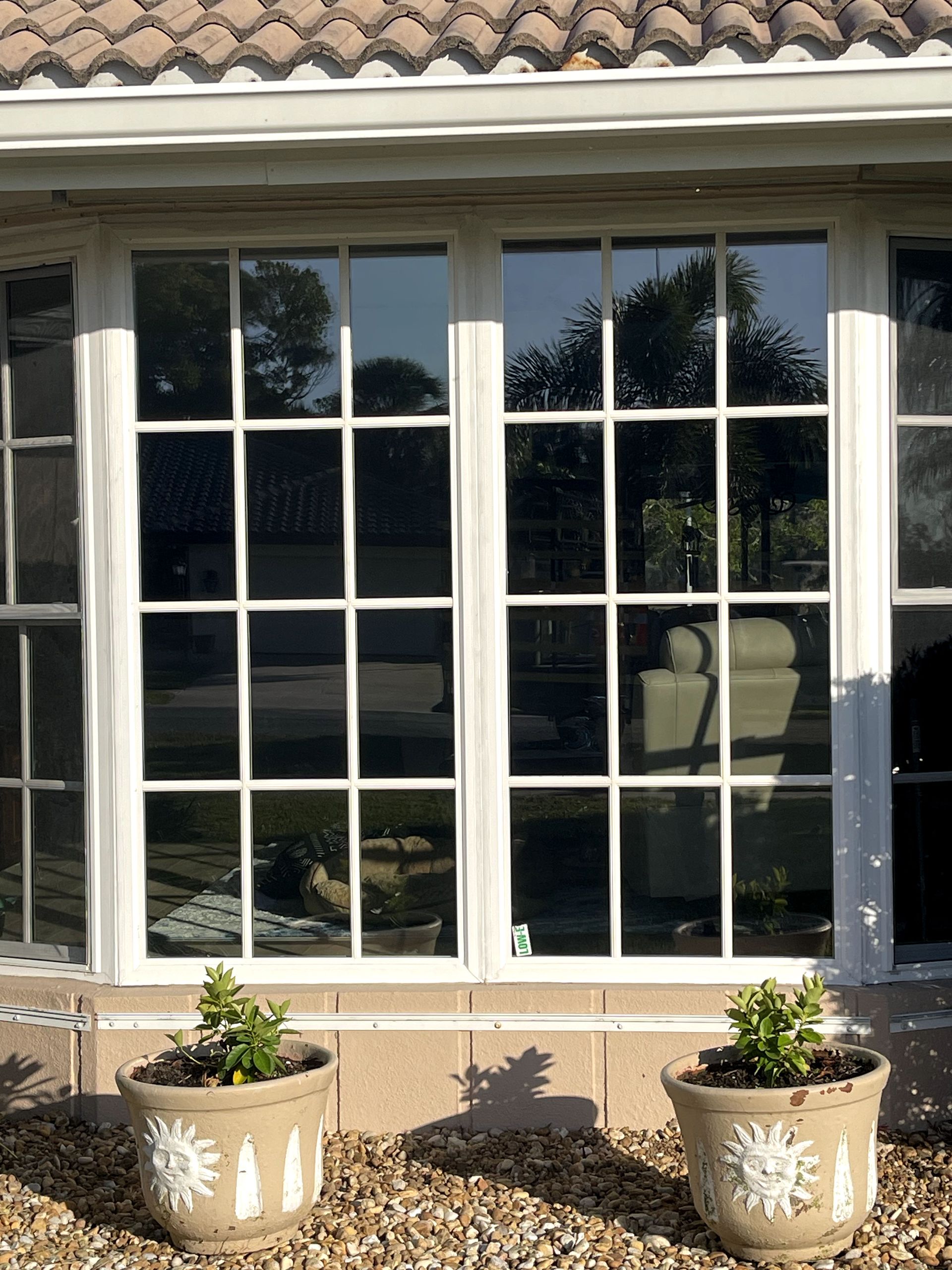 White-framed windows with dark reflective glass, two sun-design potted plants below, on a pebbled ground.