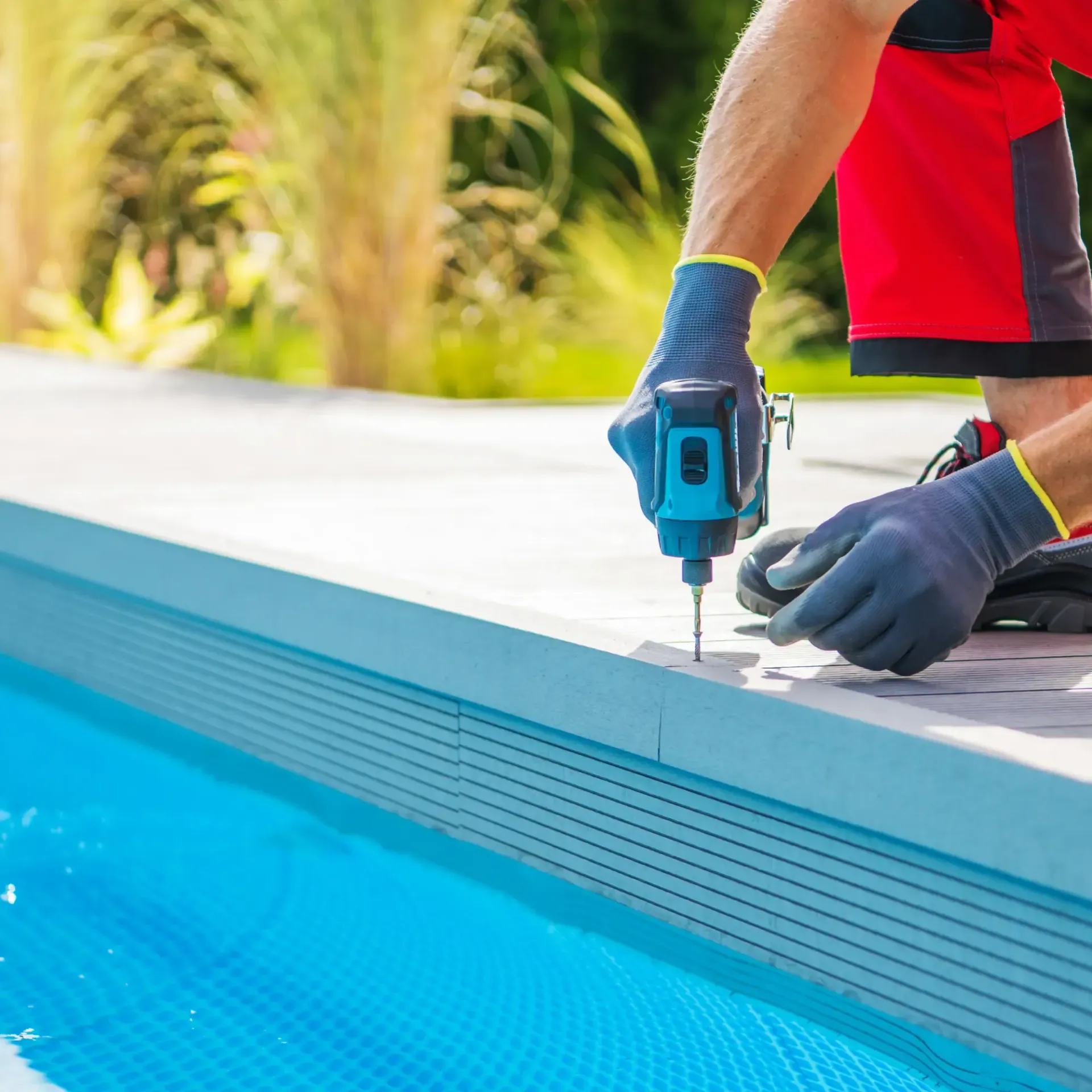 H20 Leak Solution- A man is using a drill to install a fence around a swimming pool.