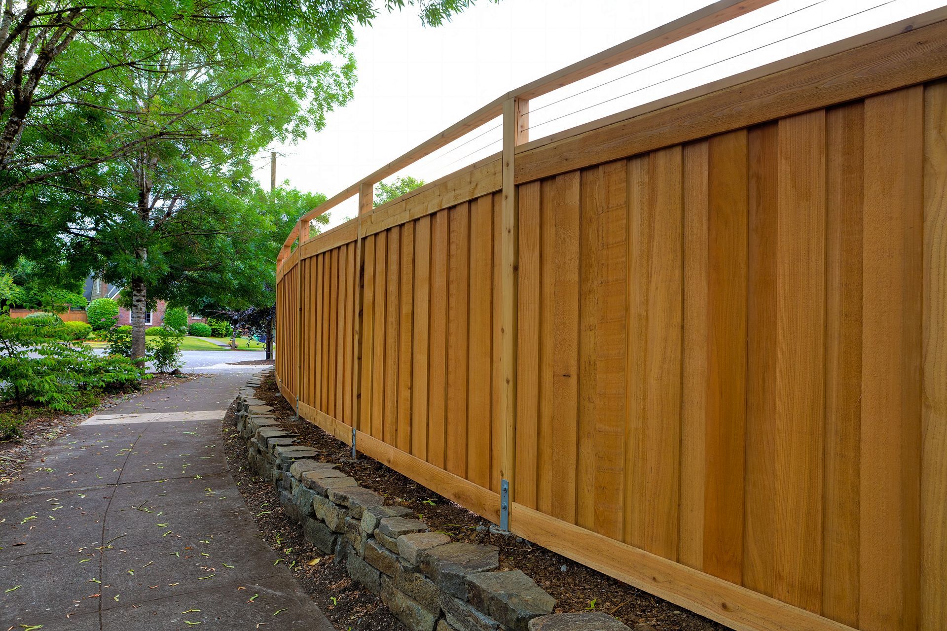Wooden fence along a winding sidewalk beside green trees in a park-like setting Wooden fence along a winding sidewalk beside green trees in a park-like setting