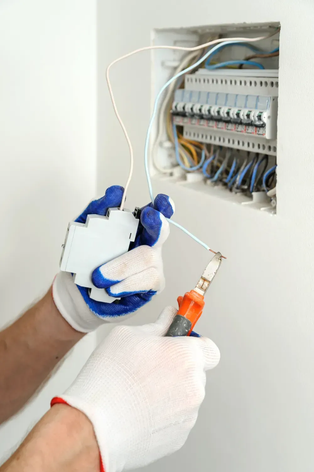 A person working on a circuit breaker box, wearing gloves, using a screwdriver.