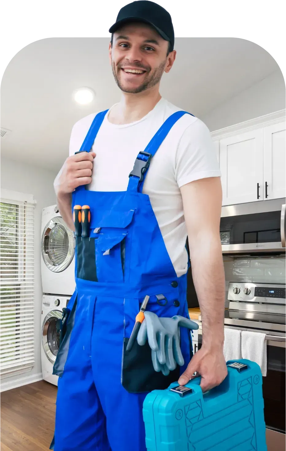 Smiling repairman in blue overalls, holding a toolbox, standing in a kitchen.