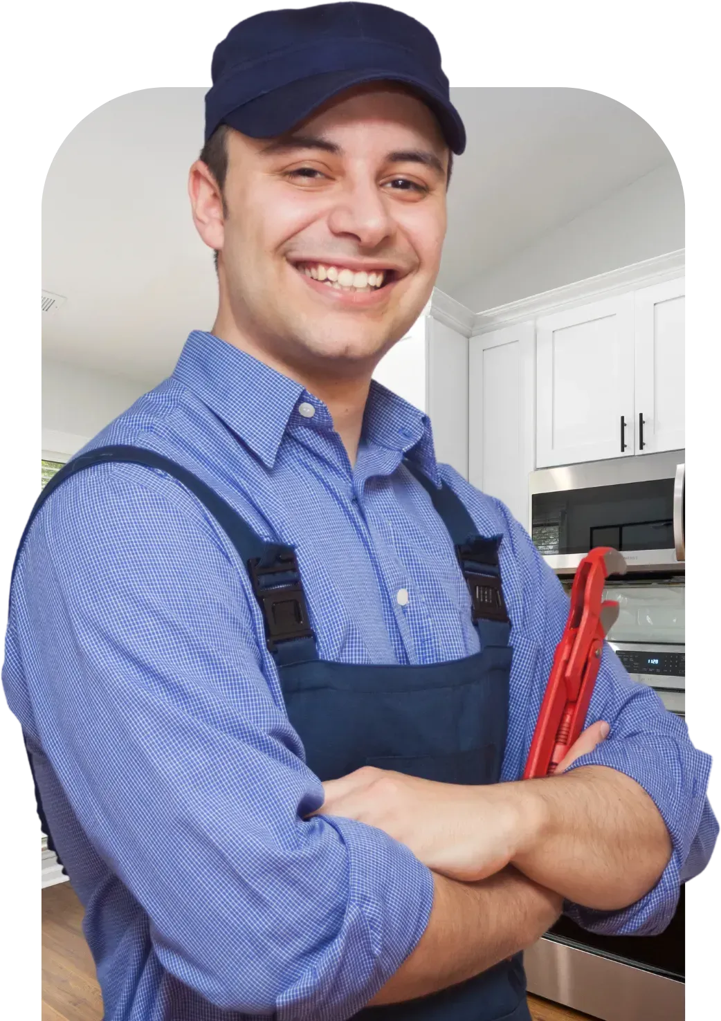 Smiling plumber in blue uniform, crossed arms, holding red wrench, in a kitchen.