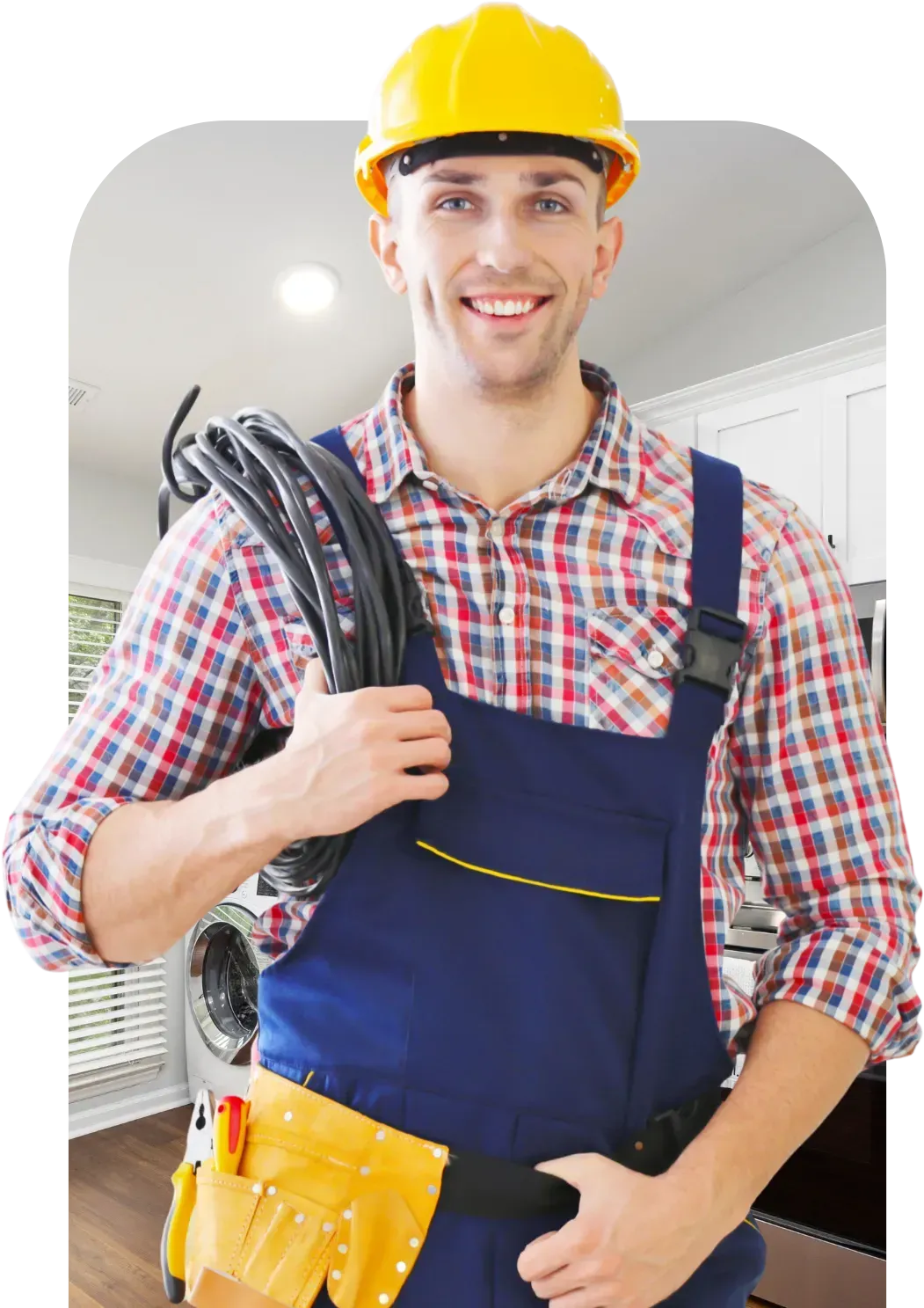 Smiling electrician in a yellow hard hat and blue overalls holds cables, standing in a kitchen.