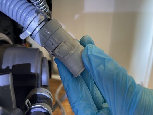 Hand in blue glove holding a light gray vacuum hose connector, next to the vacuum.
