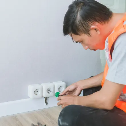 Electrician in orange vest working on electrical outlet.