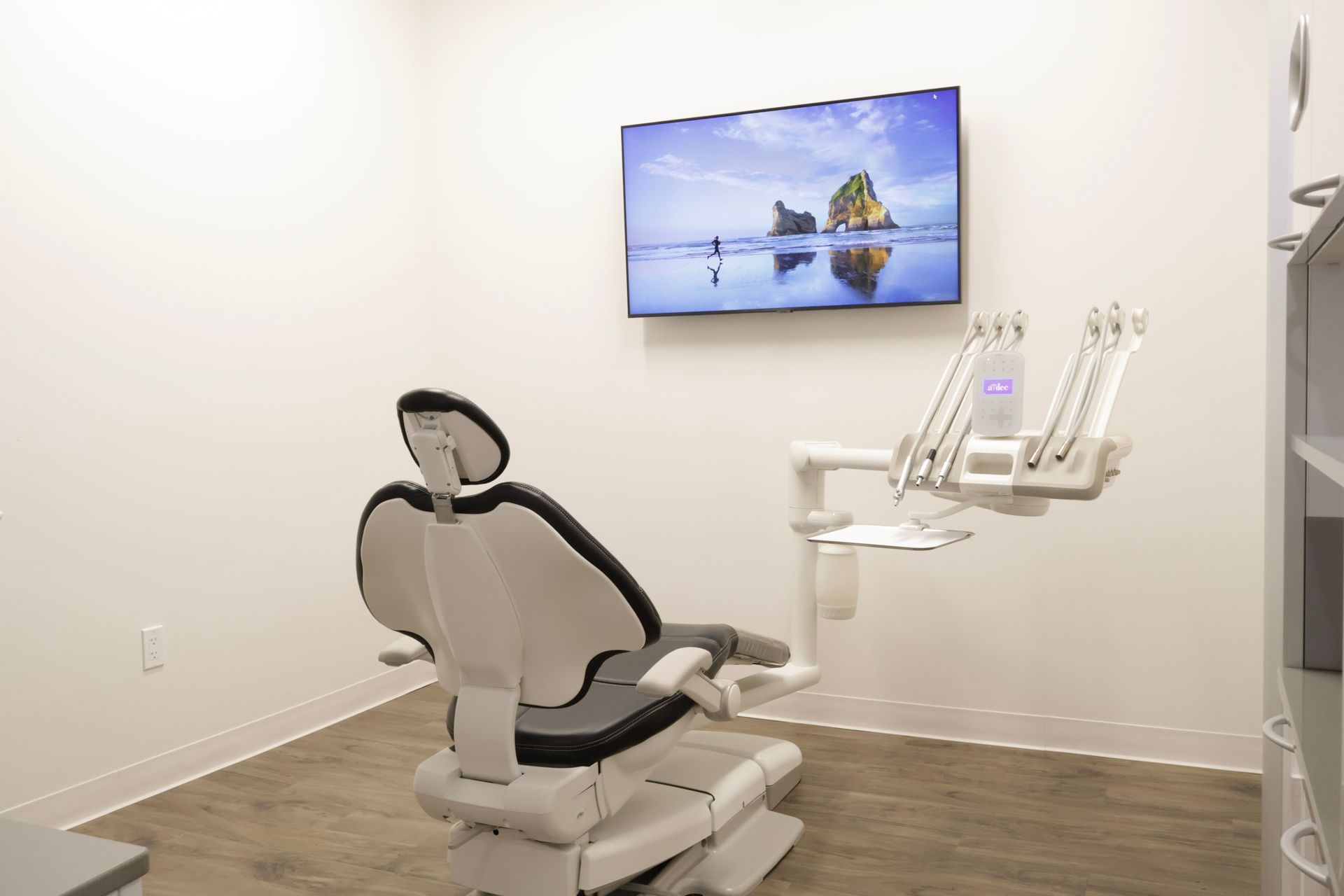 Dental examination room with chair, equipment, and a TV screen displaying a scenic view.