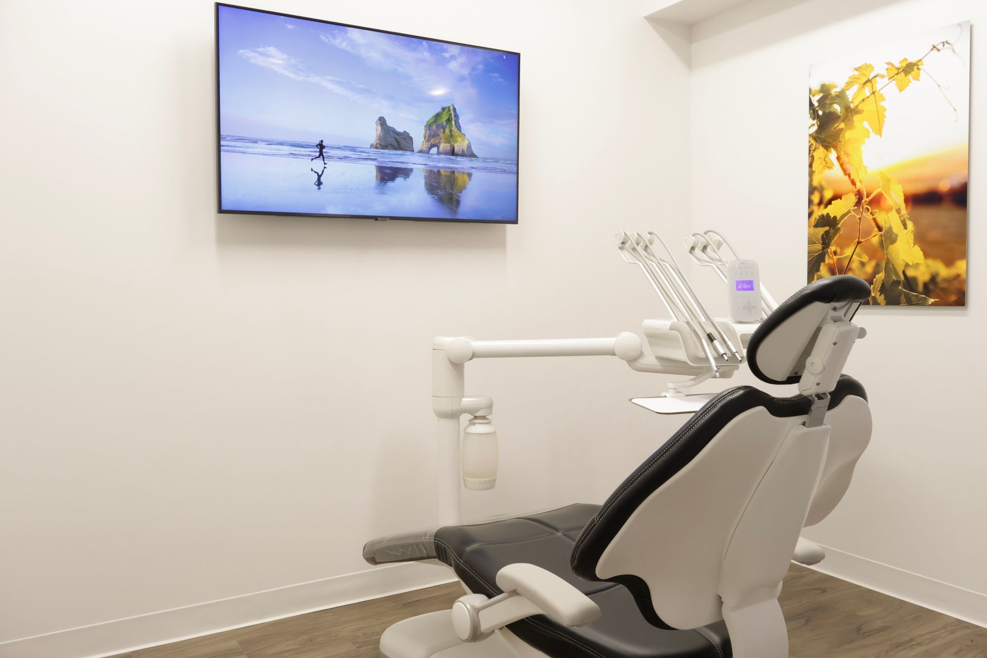 Dental office with chair and equipment, TV with ocean scene, and wall art with sunlight.