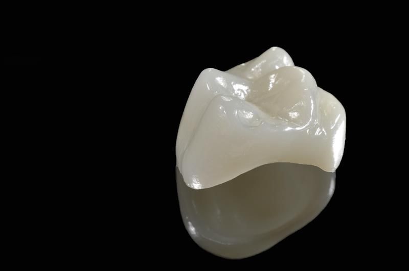 Tooth crown, light beige, resting on black surface, reflecting light.