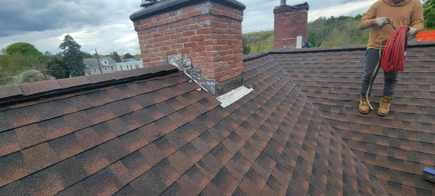 A man is standing on top of a roof next to a chimney.