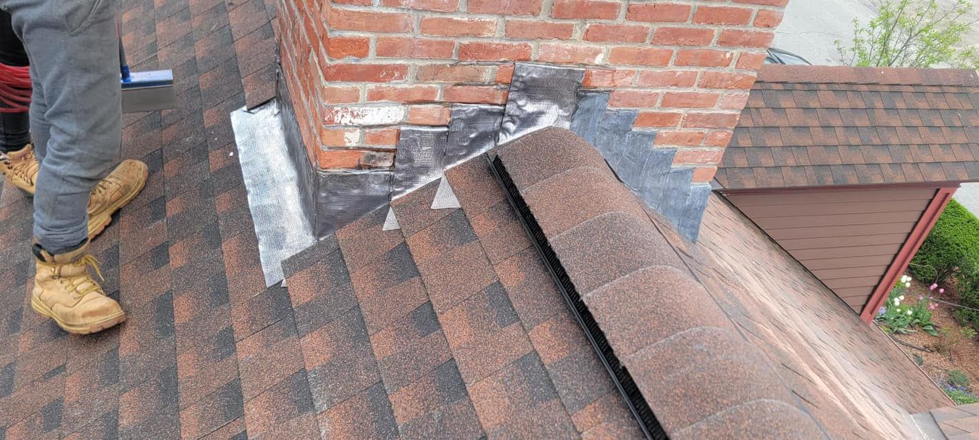 A man is standing on top of a roof next to a chimney.