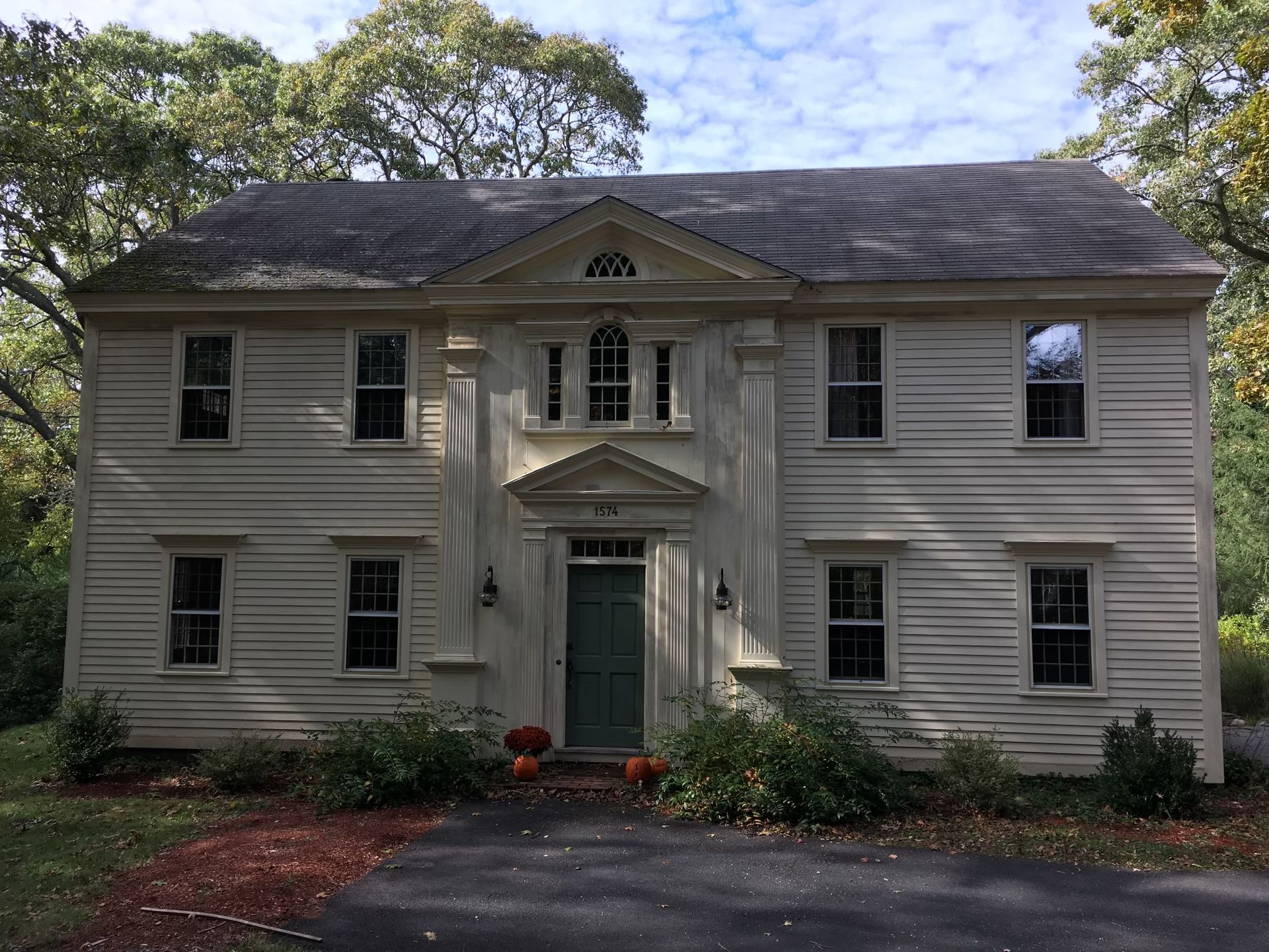 A large white house with a green door is surrounded by trees.