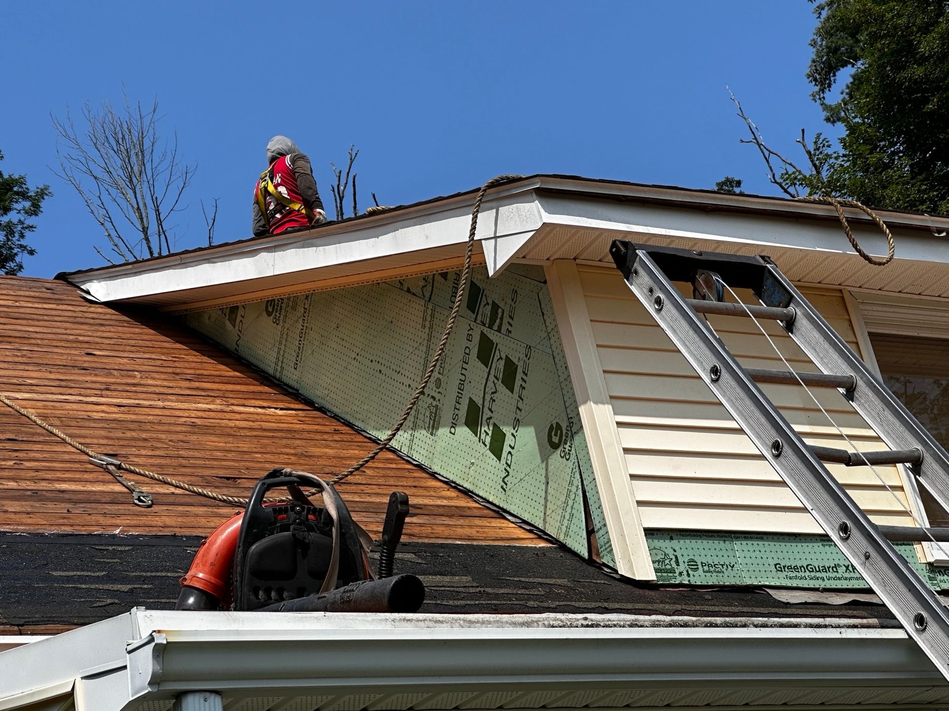 A man is working on the roof of a house with a ladder.
