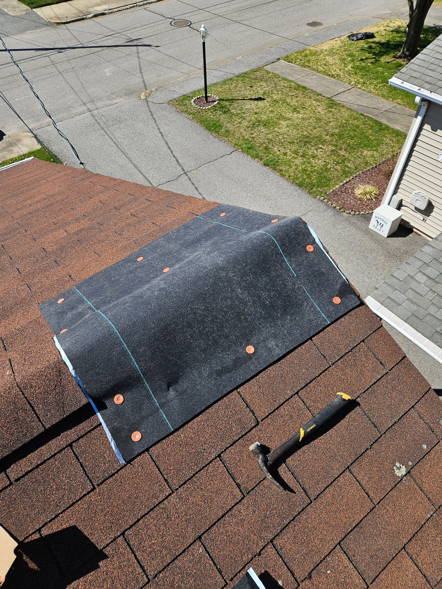 A roof with a piece of shingles and a hammer on it.