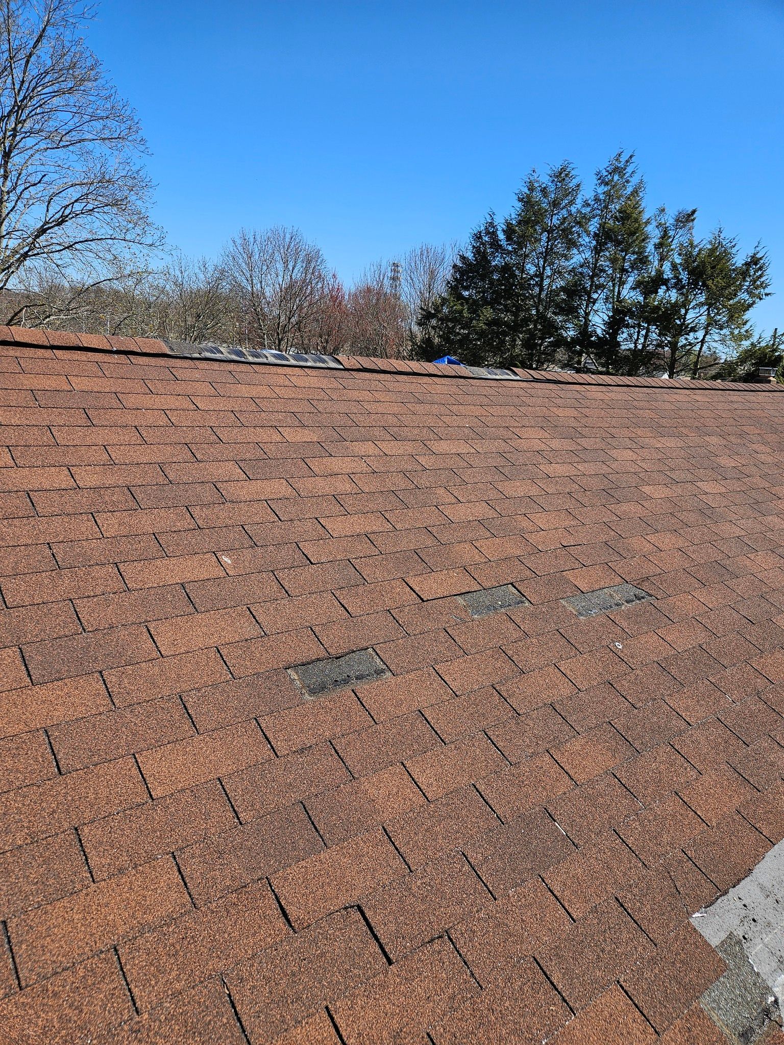 A roof with a lot of shingles on it and trees in the background.
