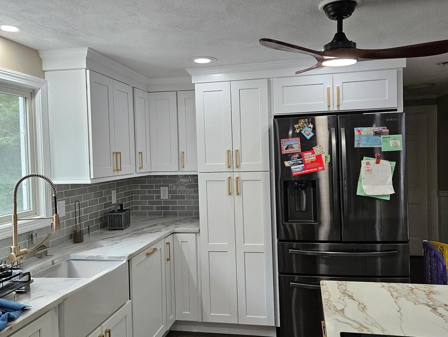A kitchen with white cabinets , a stainless steel refrigerator , a sink , and a ceiling fan.
