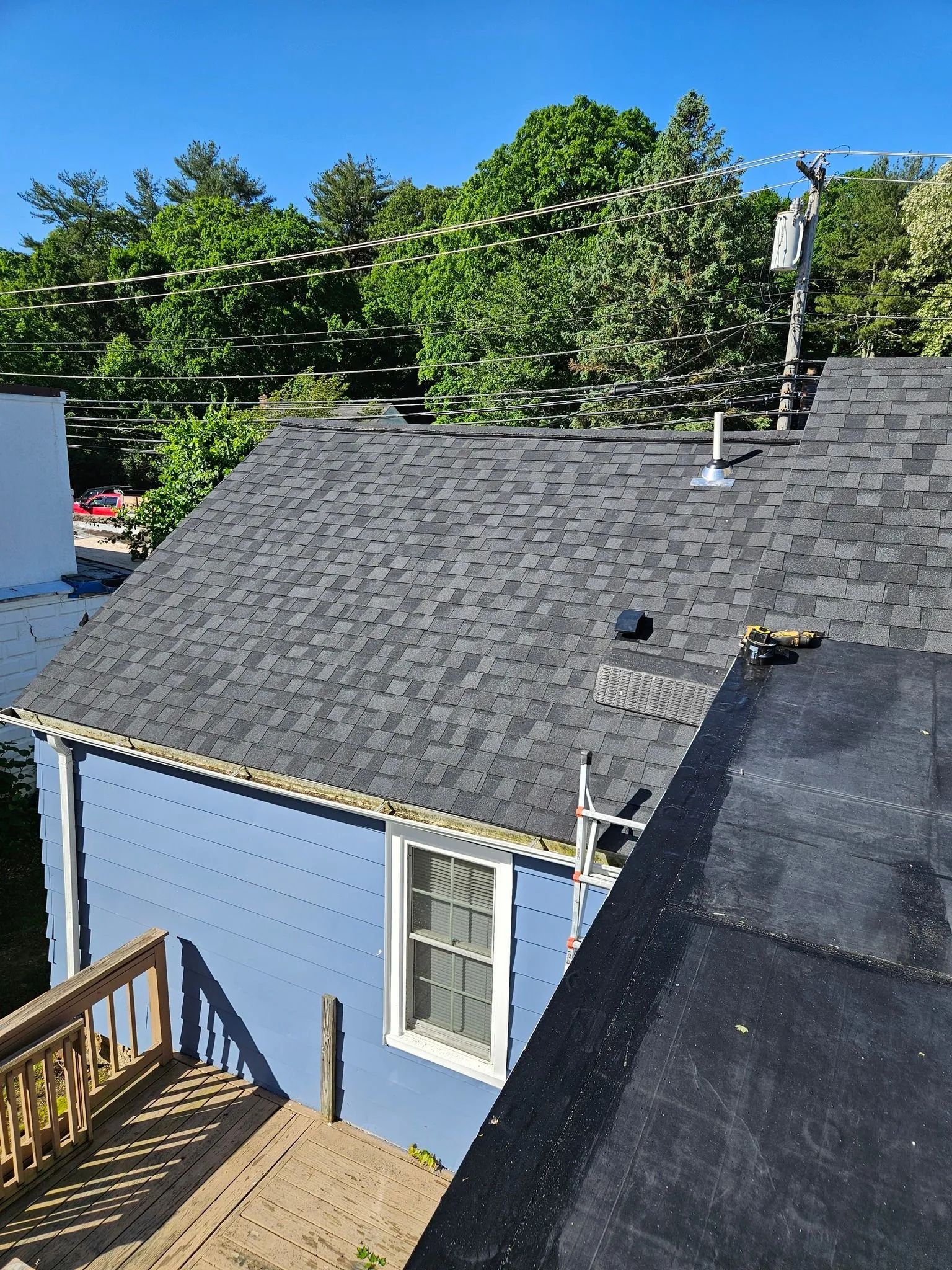 Blue house with a gray shingled roof, trees in the background, blue sky.