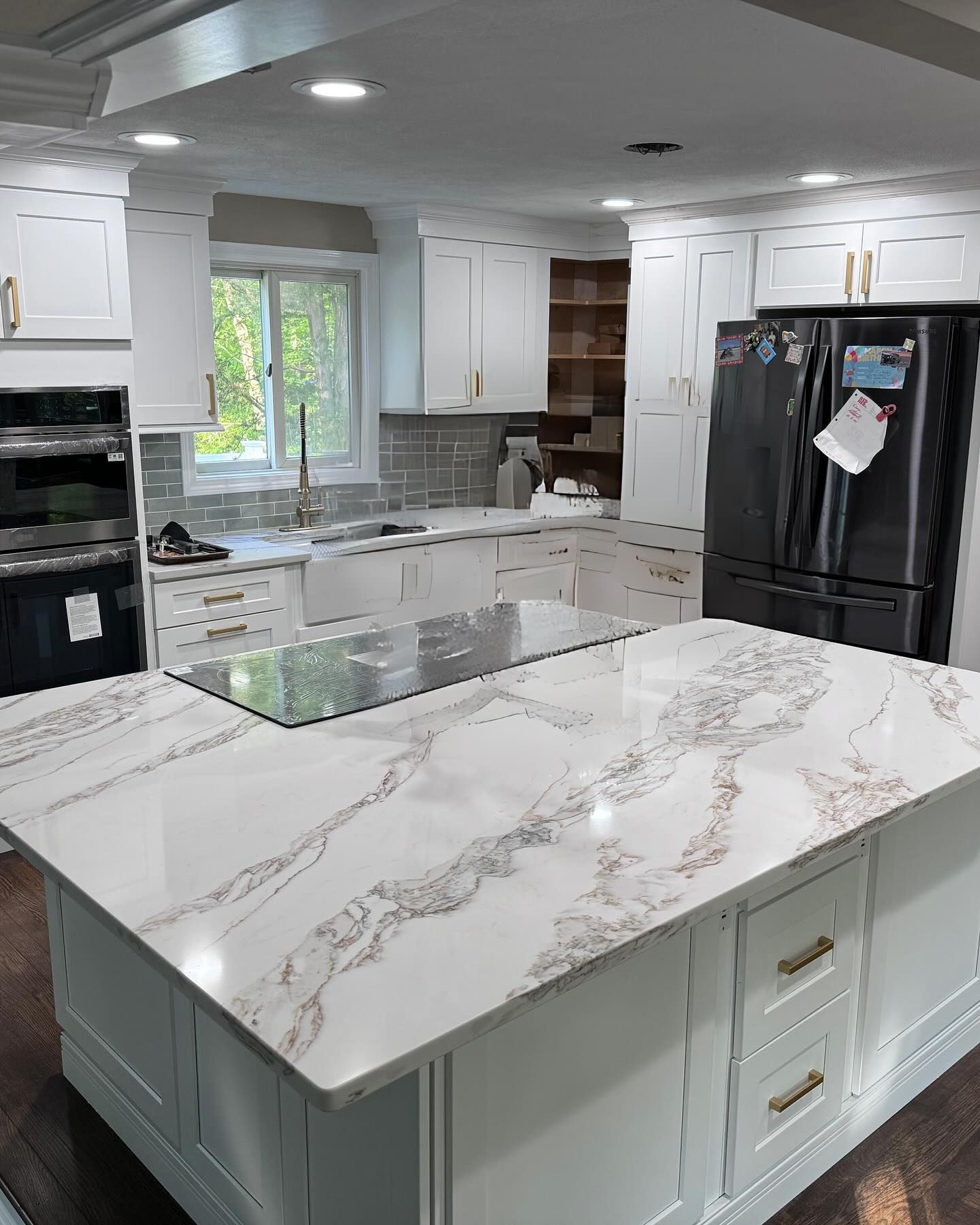 A kitchen with white cabinets , marble counter tops , a refrigerator , and a large island.