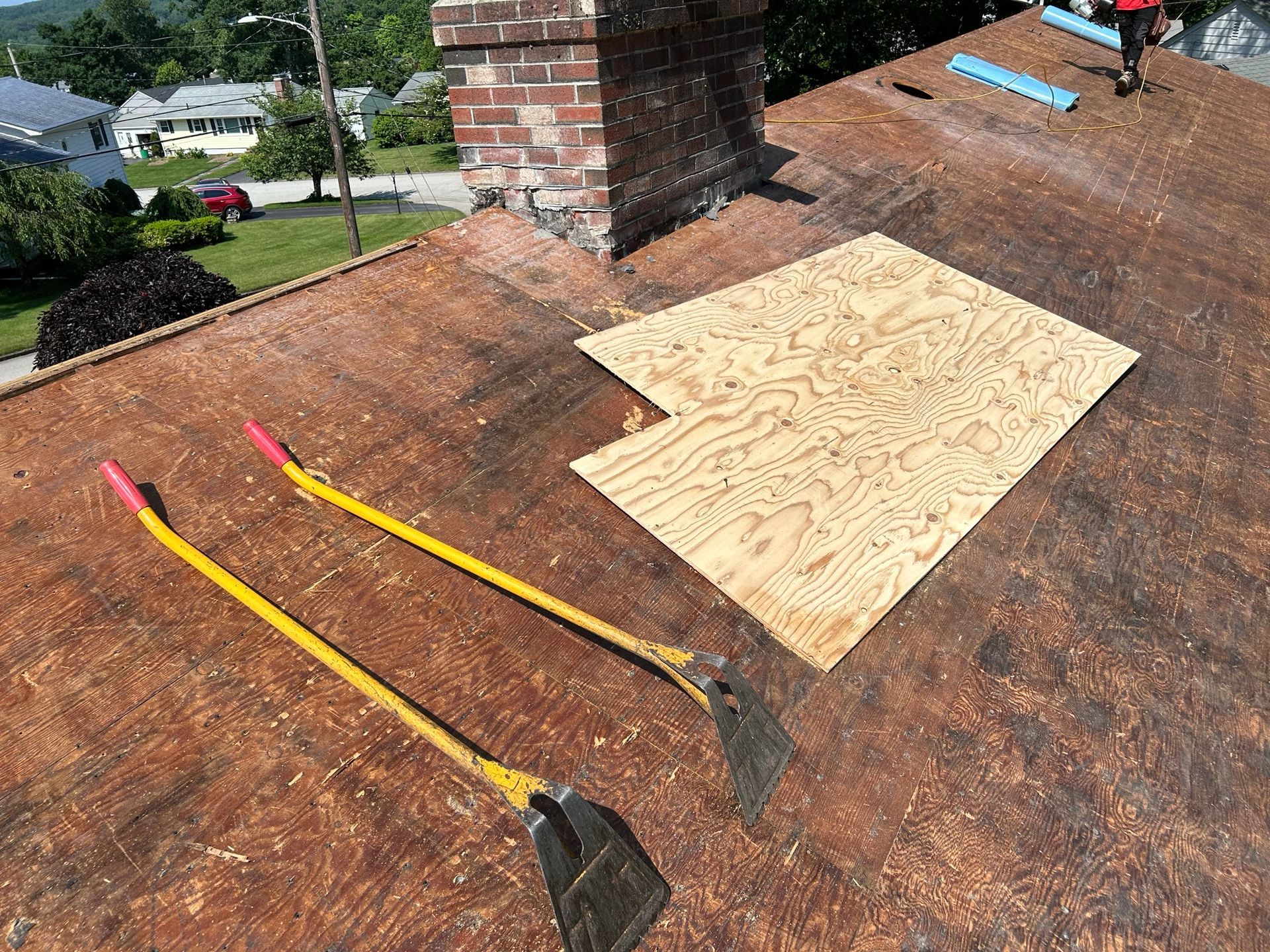 A roof with a piece of plywood and two shovels on it.