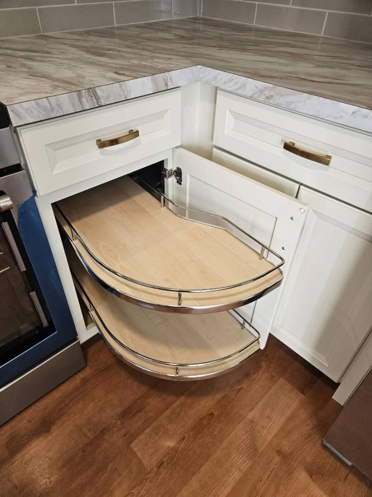 A kitchen with white cabinets and a corner cabinet with a wooden shelf.