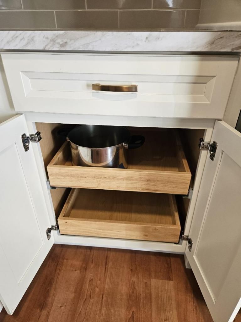 A pot is sitting in a drawer under a cabinet in a kitchen.