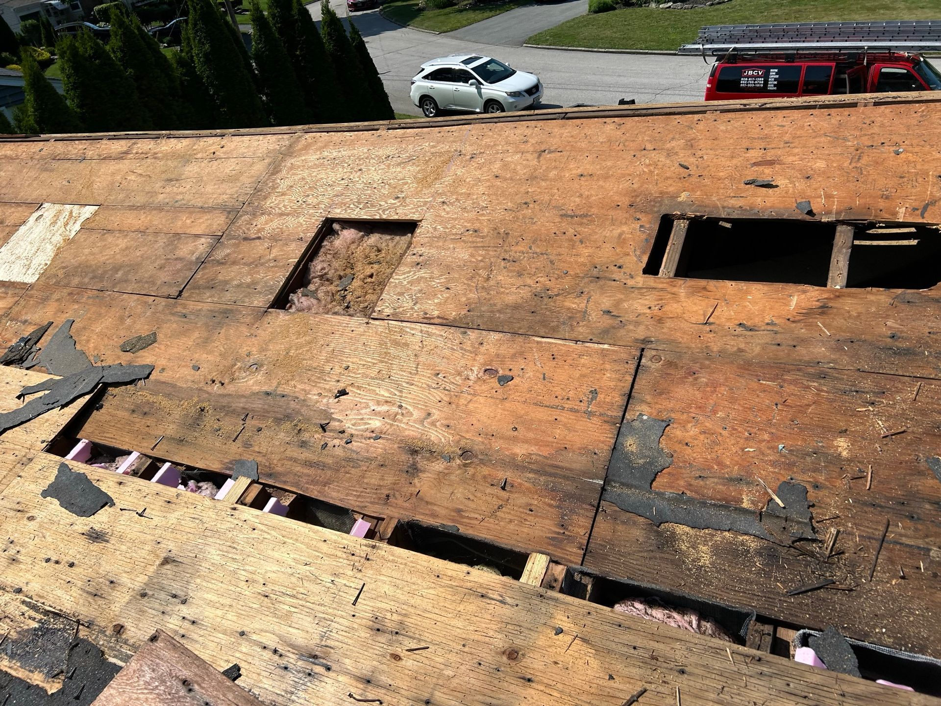 A car is parked on the side of the road next to a roof that is being repaired.