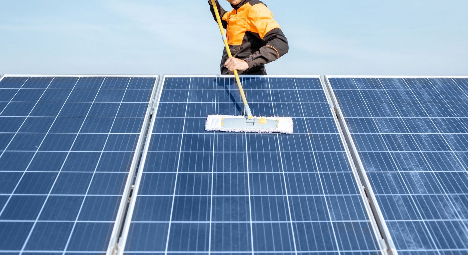A man is cleaning solar panels with a mop.