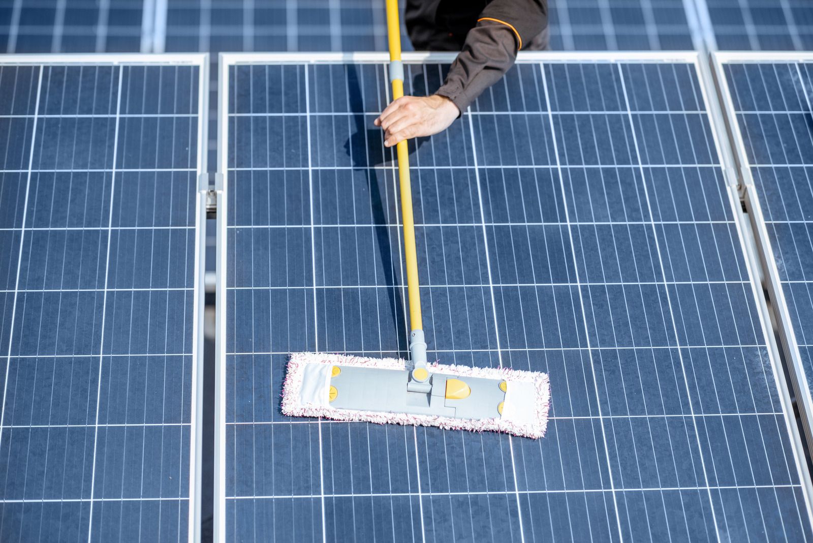 A person is cleaning solar panels with a mop.