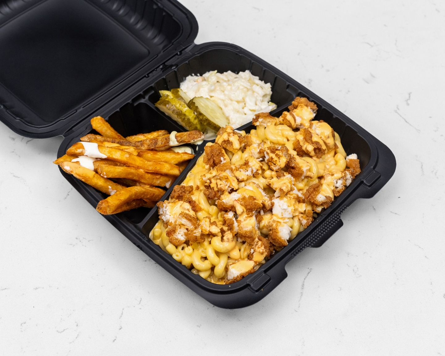 Meal with fries, mac and cheese with fried chicken, coleslaw, and pickles in a black container.