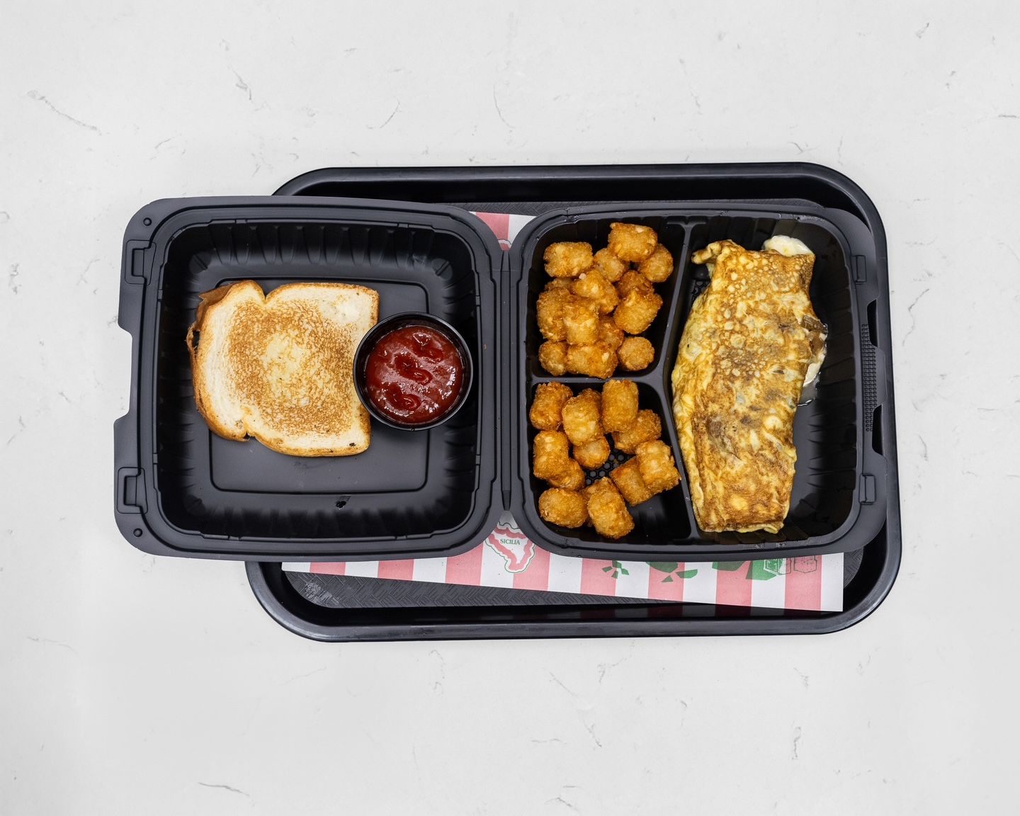 Breakfast meal in black containers: toast, ketchup, tater tots, and omelet.