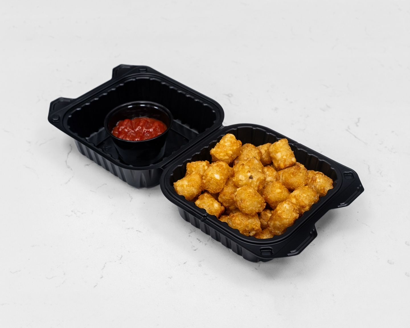 Tater tots in a black container with a side of red dipping sauce.