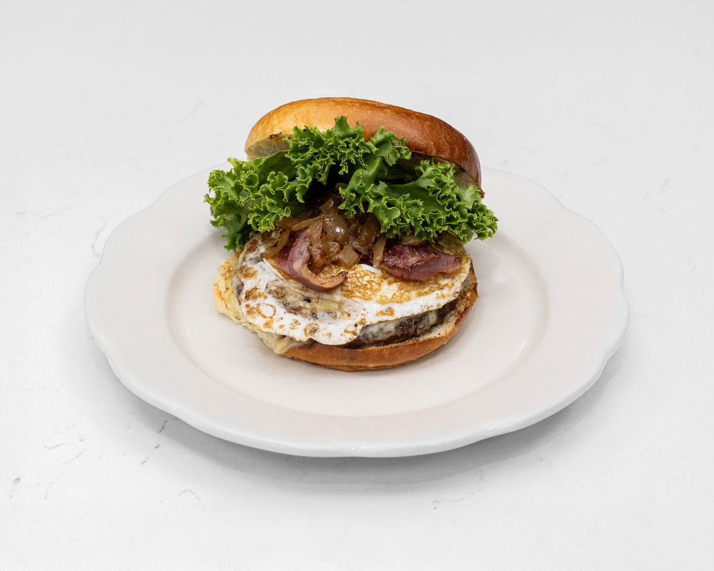 Burger with fried egg, caramelized onions, and lettuce on a white plate.