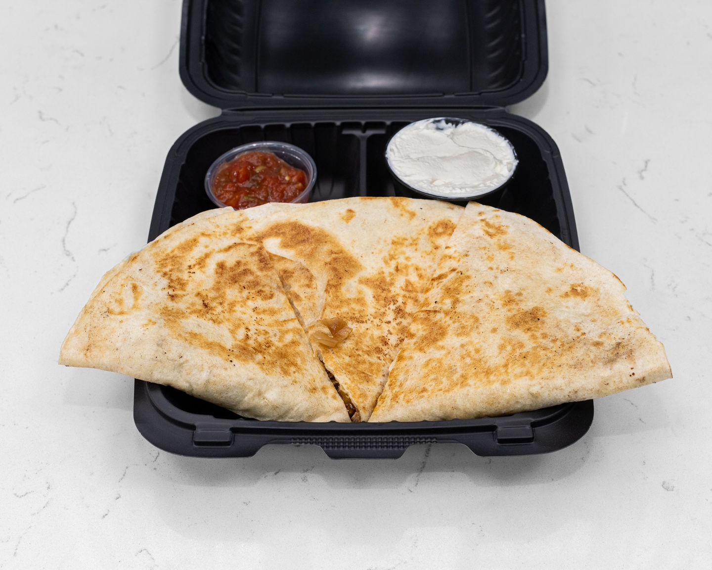 Quesadilla in black container with salsa and sour cream.