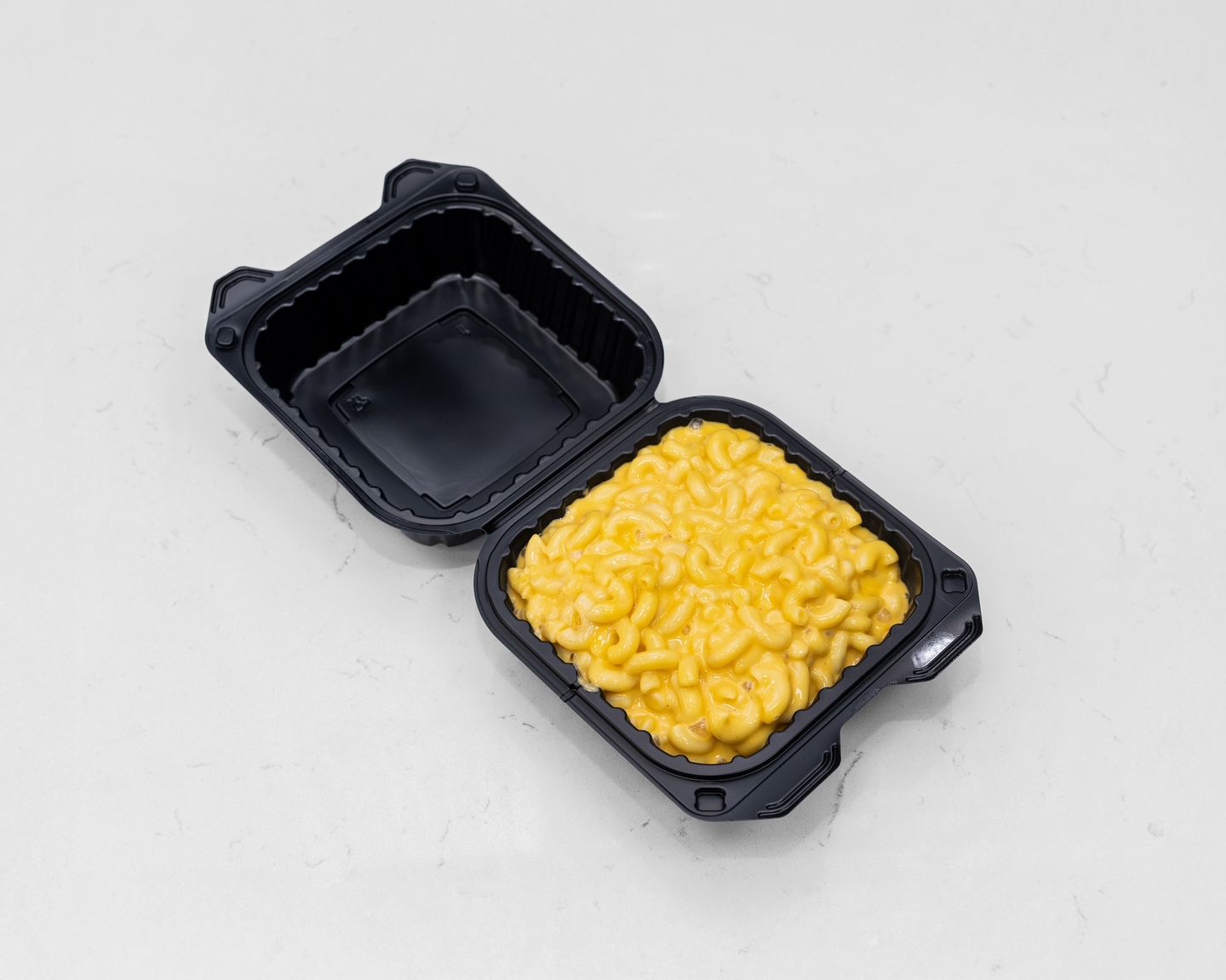 Mac and cheese in a black container, lid open, on a white surface.