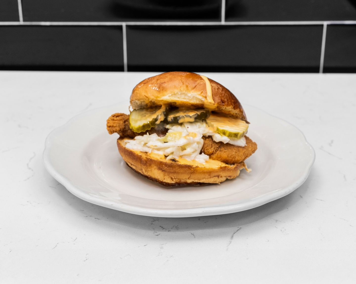 Chicken sandwich on a white plate with pickles, and coleslaw.