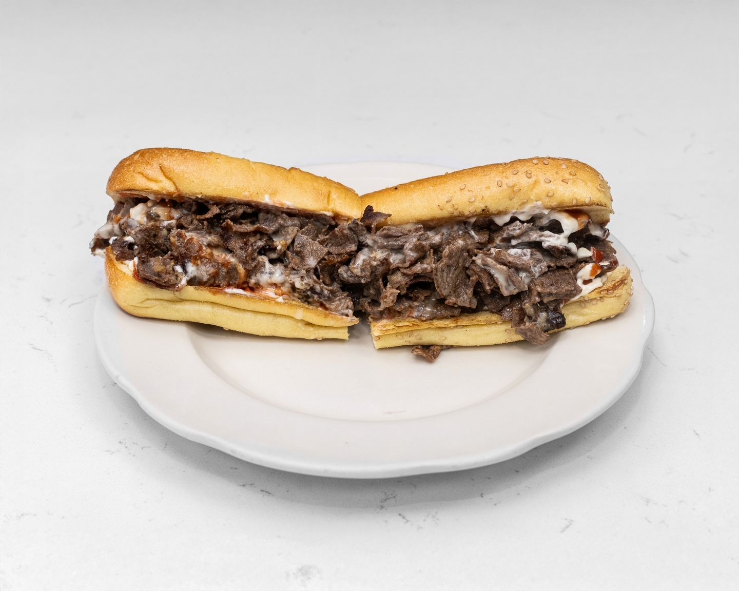 Sliced cheesesteak sandwich on a white plate, cut in half.