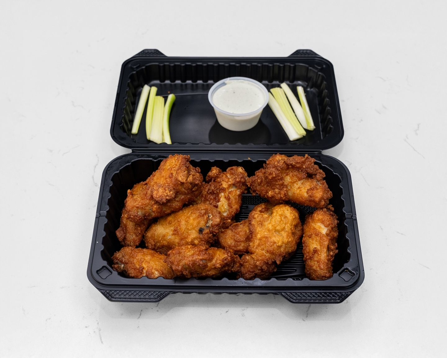 Chicken wings in a black container with celery and dipping sauce.