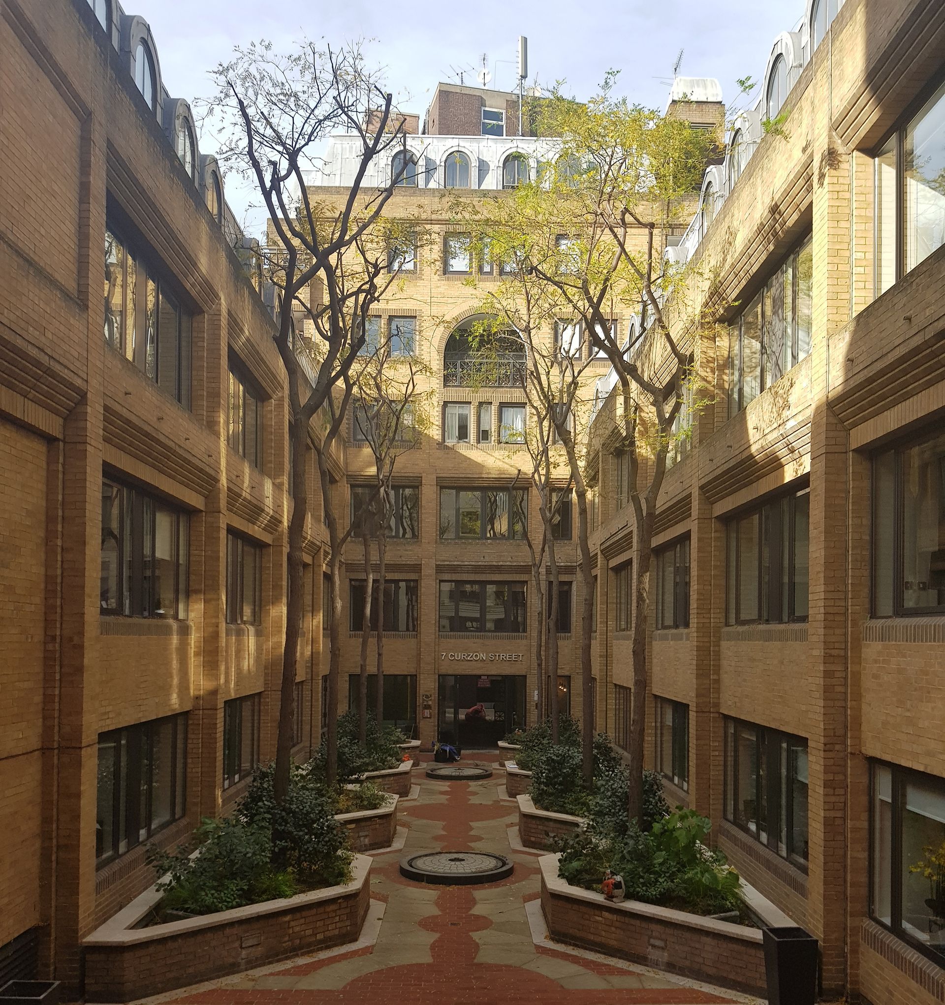 Brick courtyard with trees, shrubs, and building facades.