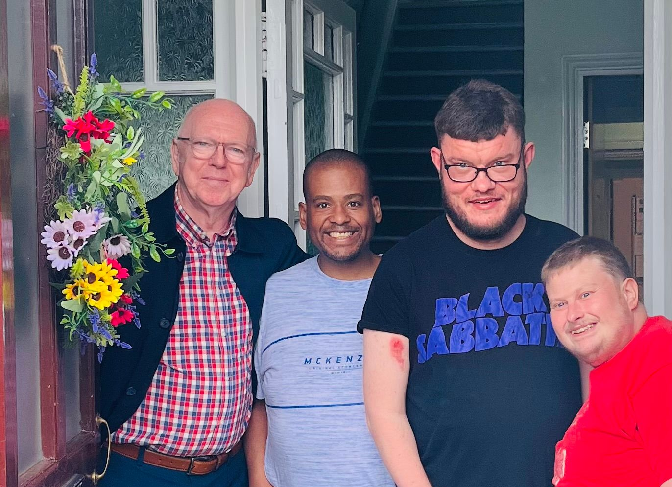 Myles Kelly, PWSA project manager standing at the front door with three young men with Prader-Willi syndrome 
