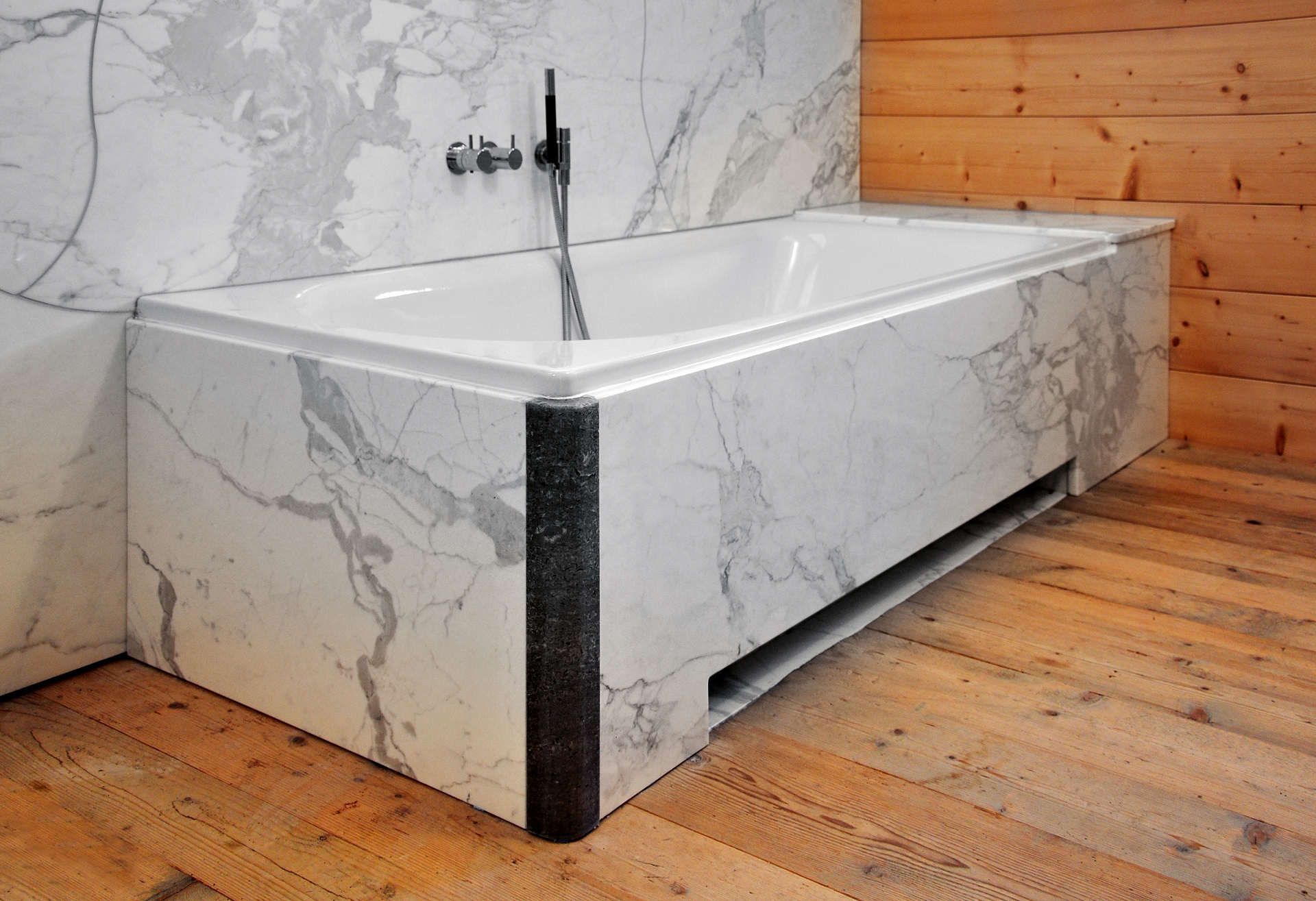 Eine Badewanne in einem Badezimmer mit Marmorwänden und Holzböden.