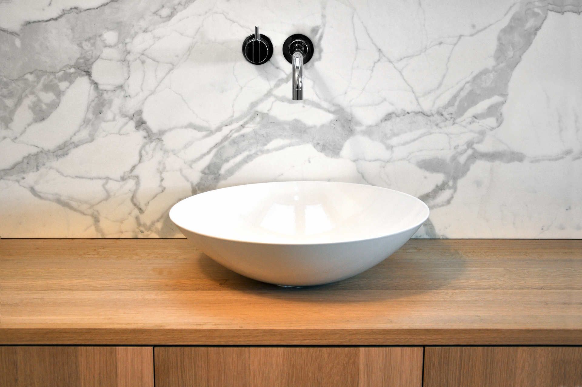 In einem Badezimmer steht ein weißes Waschbecken auf einer Holzablage.