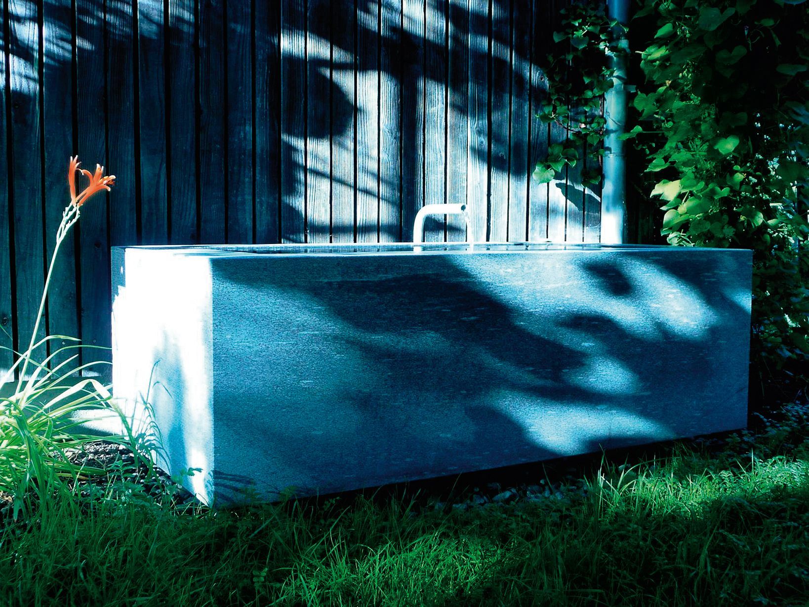 Eine blaue Badewanne steht im Gras vor einem Holzzaun