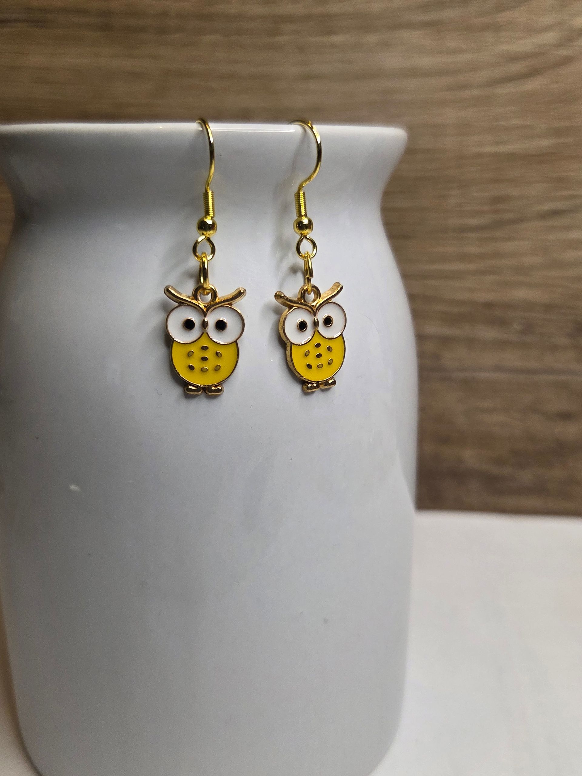 Een paar gele uilenoorbellen hangen aan een witte vaas.